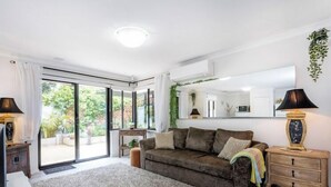 A living room with a sofa, a coffee table, a lamp, and a sliding glass door leading to a garden.