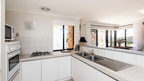 A modern kitchen with white cabinets, a gas stove, a microwave, and a sink.