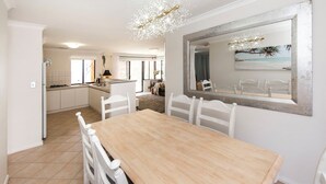 A modern kitchen with white cabinetry, a wooden dining table, and a chandelier.