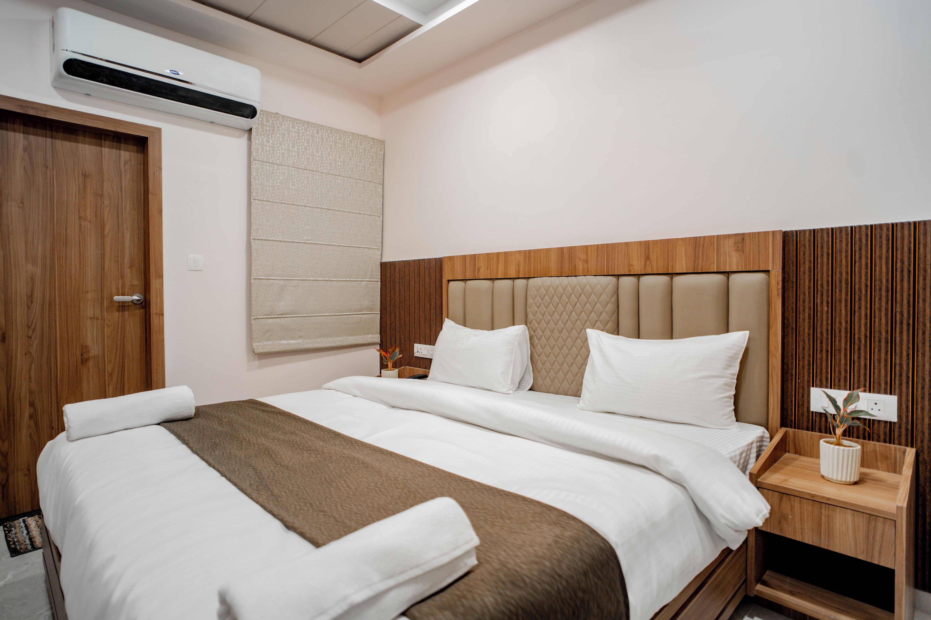 A hotel room with a large bed, a wooden headboard, a bedside table, and an air conditioning unit.