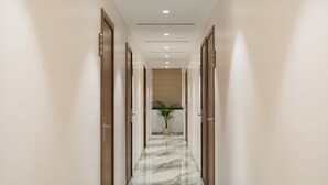 A corridor with marble flooring and wooden doors, leading to a room with a plant. - Hotel SK Elite (Jodhpur)