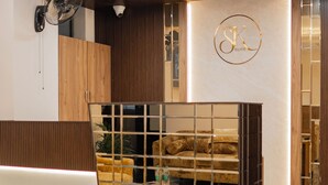 A modern hotel lobby with a marble floor, a sofa, a chair, a fan, and a decorative wall with a logo. - Hotel SK Elite (Jodhpur)