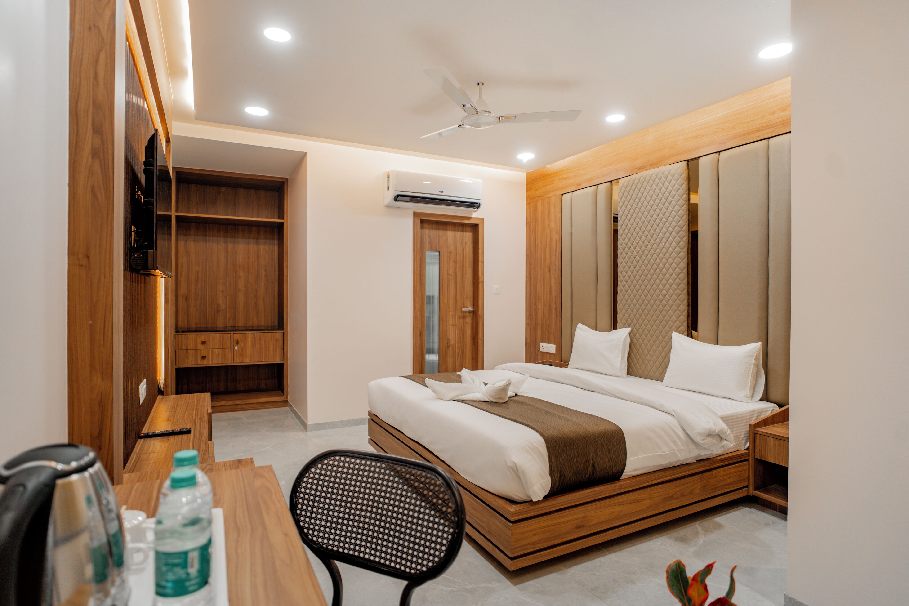 A modern hotel room with a wooden bed, a desk with a chair, a TV, and a wardrobe.