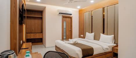 A modern hotel room with a wooden bed, a desk with a chair, a TV, and a wardrobe.