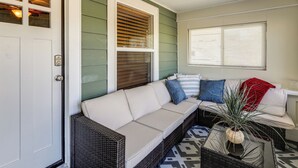 A room with a white sofa, a wicker chair, a patterned rug, and a window with blinds. - Route 66 Retreat: Dog-Friendly Home in Williams (Williams)