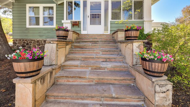 A house with a front porch, a set of stone steps leading to a door, and two large flower pots on either side of the steps. - Route 66 Retreat: Dog-Friendly Home in Williams (Williams)