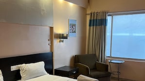 Ein Hotelzimmer mit einem großen Bett, einem Sessel, einem kleinen Tisch und einem Fenster mit Vorhängen.