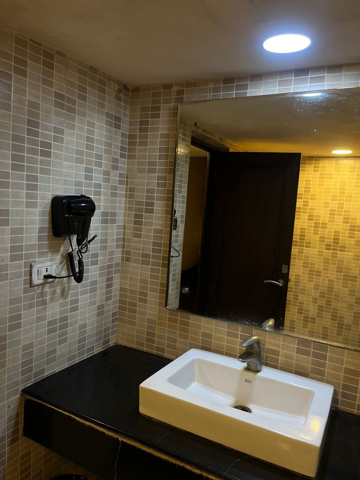 Un baño con lavamanos blanco, un espejo y un secador de pelo fijado a la pared.