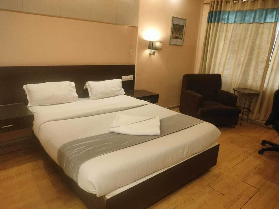 A hotel room with a large bed, a chair, a nightstand, and a wall-mounted lamp.