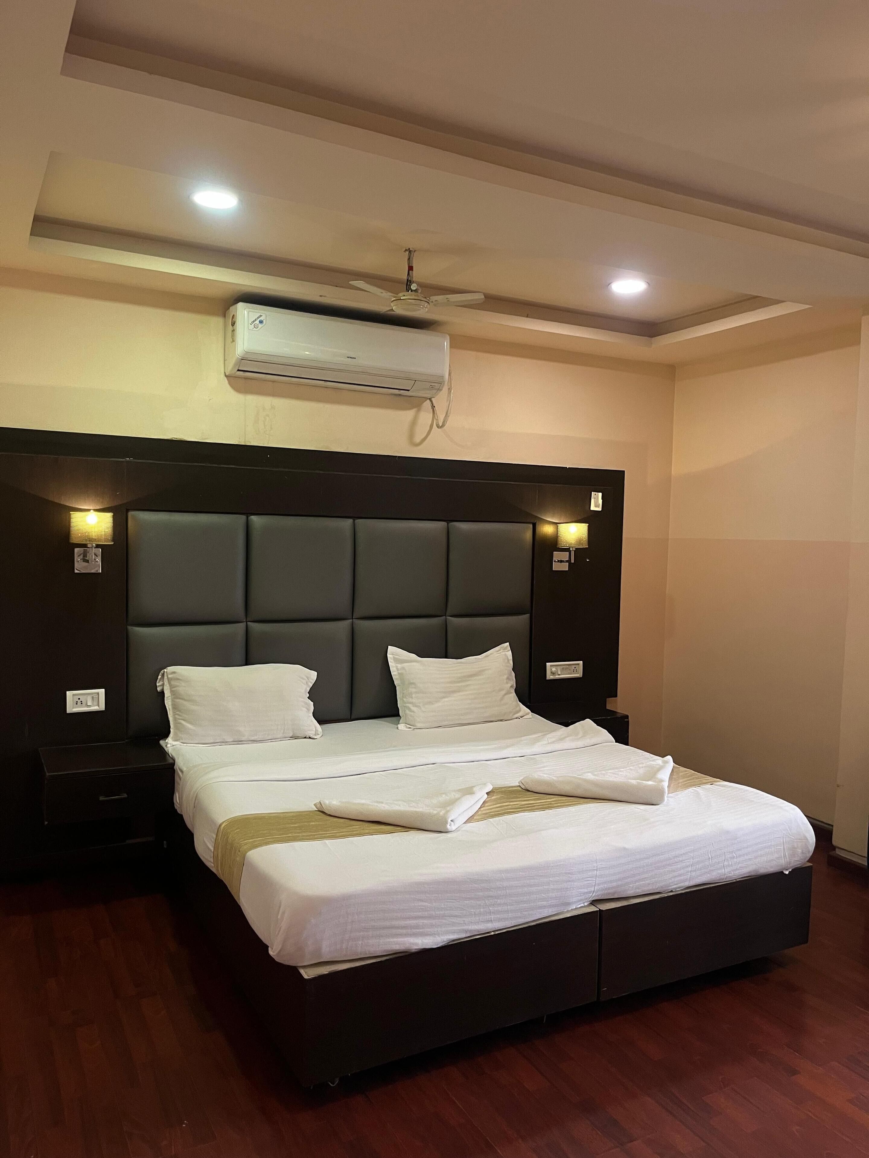 Habitación de hotel con una cama grande, cabecero oscuro, lámparas de noche, unidad de aire acondicionado y ventilador de techo.