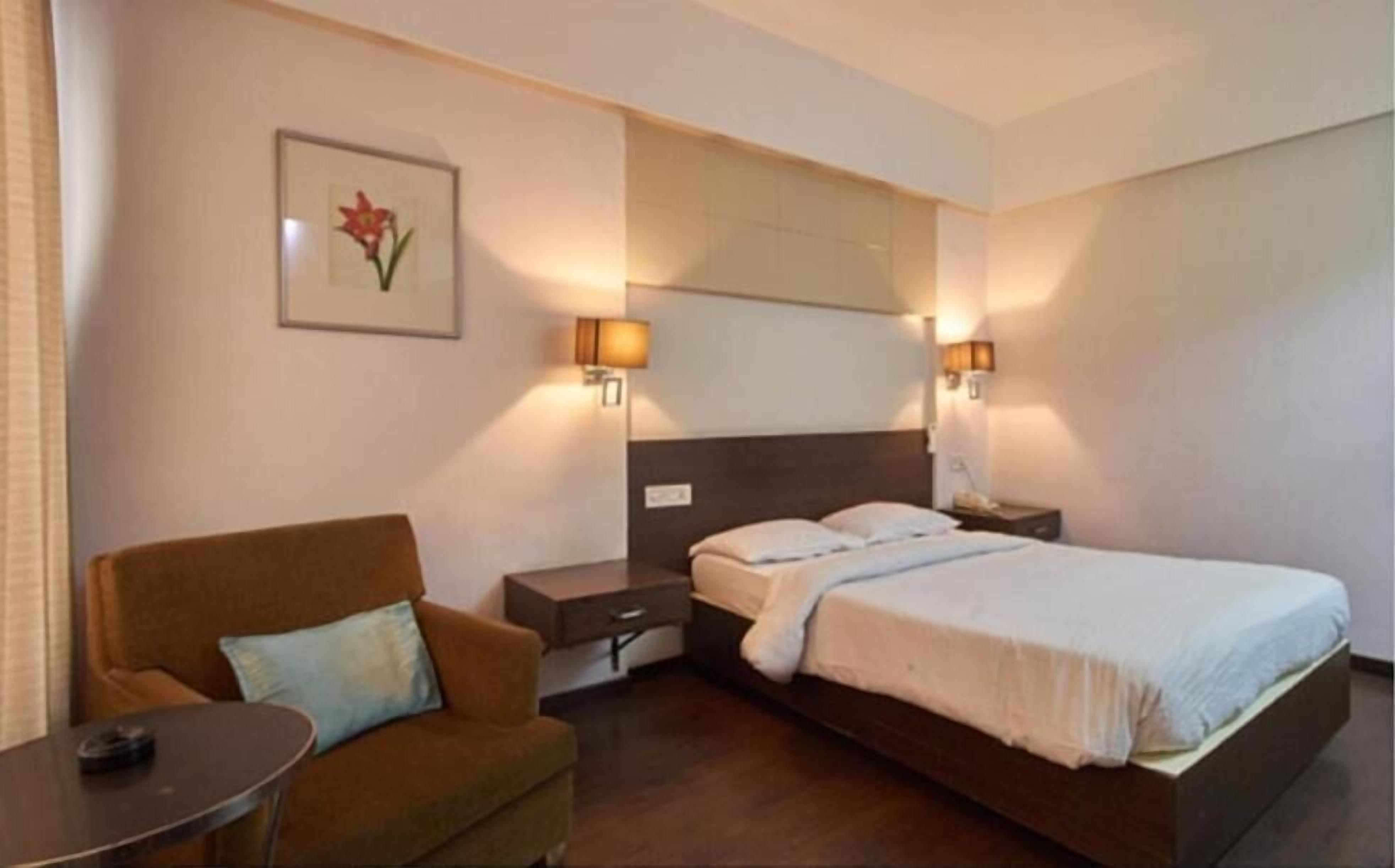 A hotel room with a bed, a sofa, a nightstand, and a lamp.