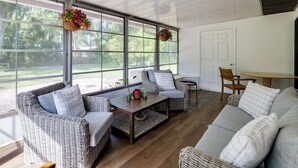 Un solárium con mobiliario de mimbre, ventanas amplias y cestas de flores colgantes.