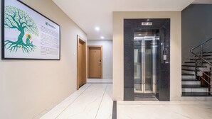 En moderne gang med marmorgulv, et indrammet trætryk, elevator og trappe.