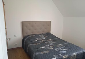 Un dormitorio con cabecera capitonada, colcha estampada y suelo de madera.