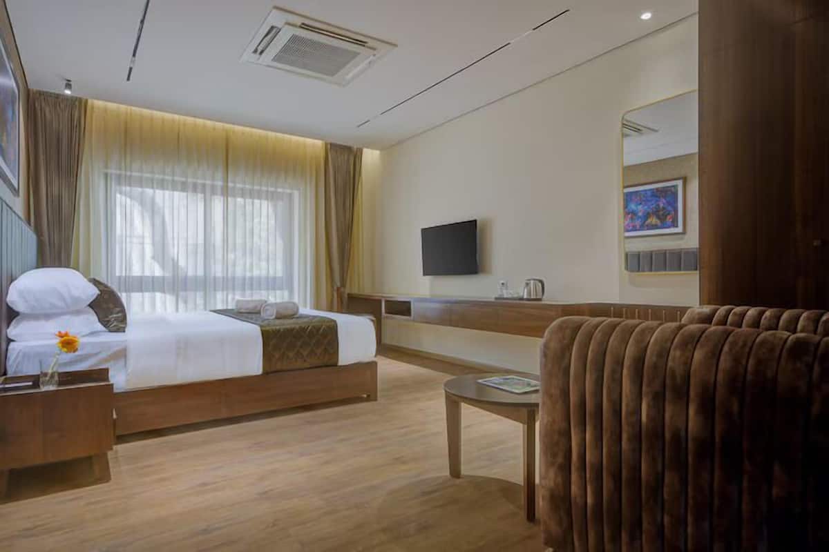 A hotel room with a bed, bedside table, a small round table, a sofa, a TV, and a window with curtains.