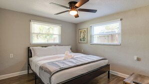 Un dormitorio con una cama, un ventilador de techo y dos ventanas con persianas.