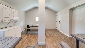 Una habitación con piso de madera, un área de cocina con armarios, una mesa y un banco.