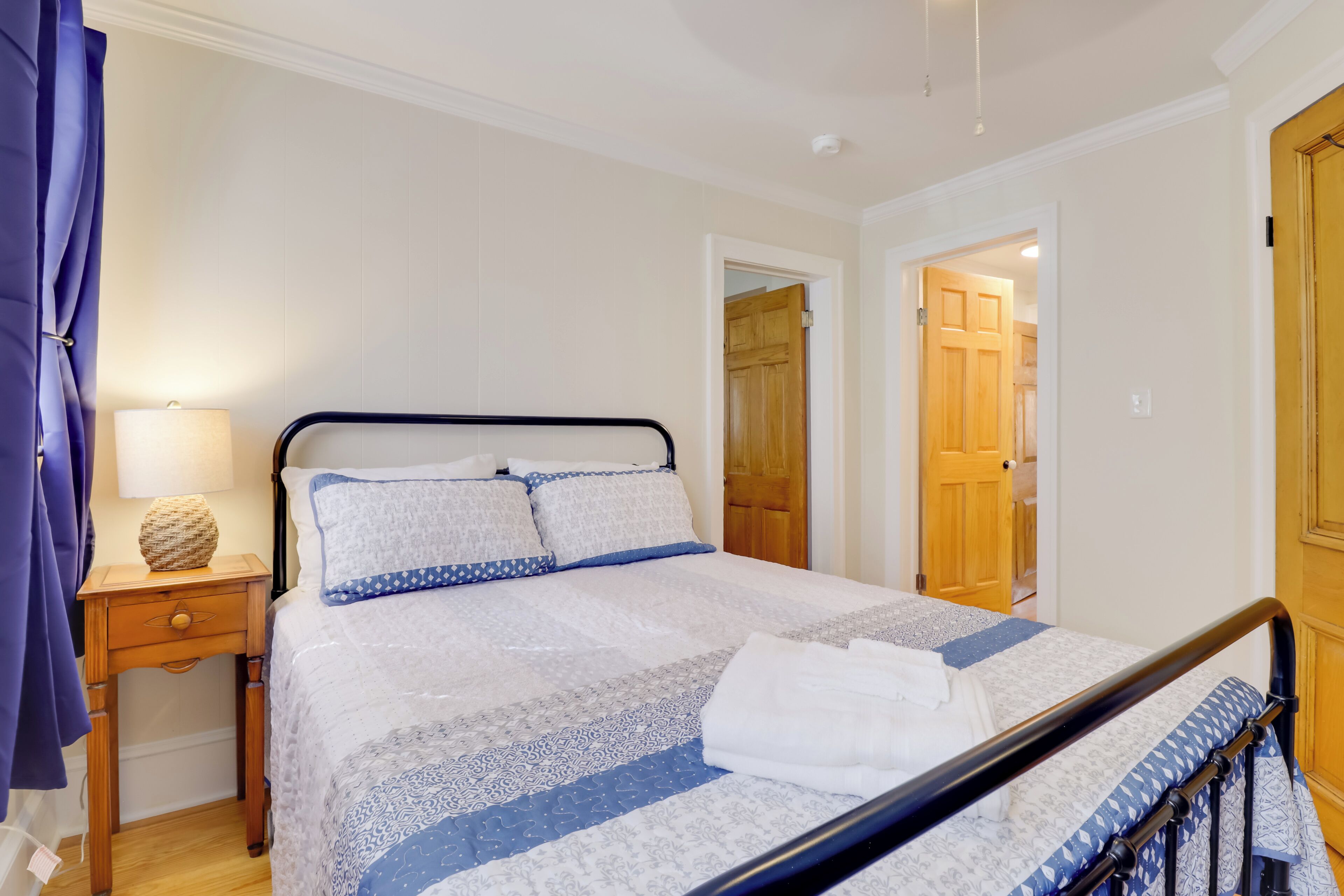 Un letto rifatto con una coperta a motivi, un comodino con una lampada e una porta in legno sullo sfondo.