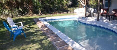 A swimming pool with a stone border, surrounded by grass and trees.