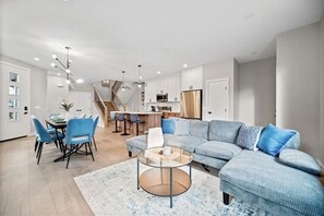 Uma sala de estar moderna com um sofá seccional, uma mesa de centro e uma área de jantar com cadeiras.