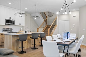 Una cucina moderna con isola centrale, sgabelli da bar, un tavolo da pranzo per quattro persone e una scala che conduce a un altro piano.
