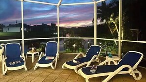 A covered outdoor seating area with lounge chairs and a table, overlooking a scenic landscape. - Gulf Access•Sunset Views•Heated Pool•Kayaks•Arcade (Cape Coral)