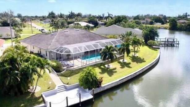A house with a swimming pool, surrounded by a waterway and palm trees. - Gulf Access•Sunset Views•Heated Pool•Kayaks•Arcade (Cape Coral)