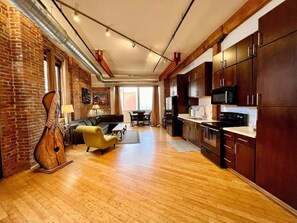 A spacious living area with a wooden floor, a sofa, a dining table, and a kitchen area with dark cabinets and a microwave. - Music City Lofts (Nashville)