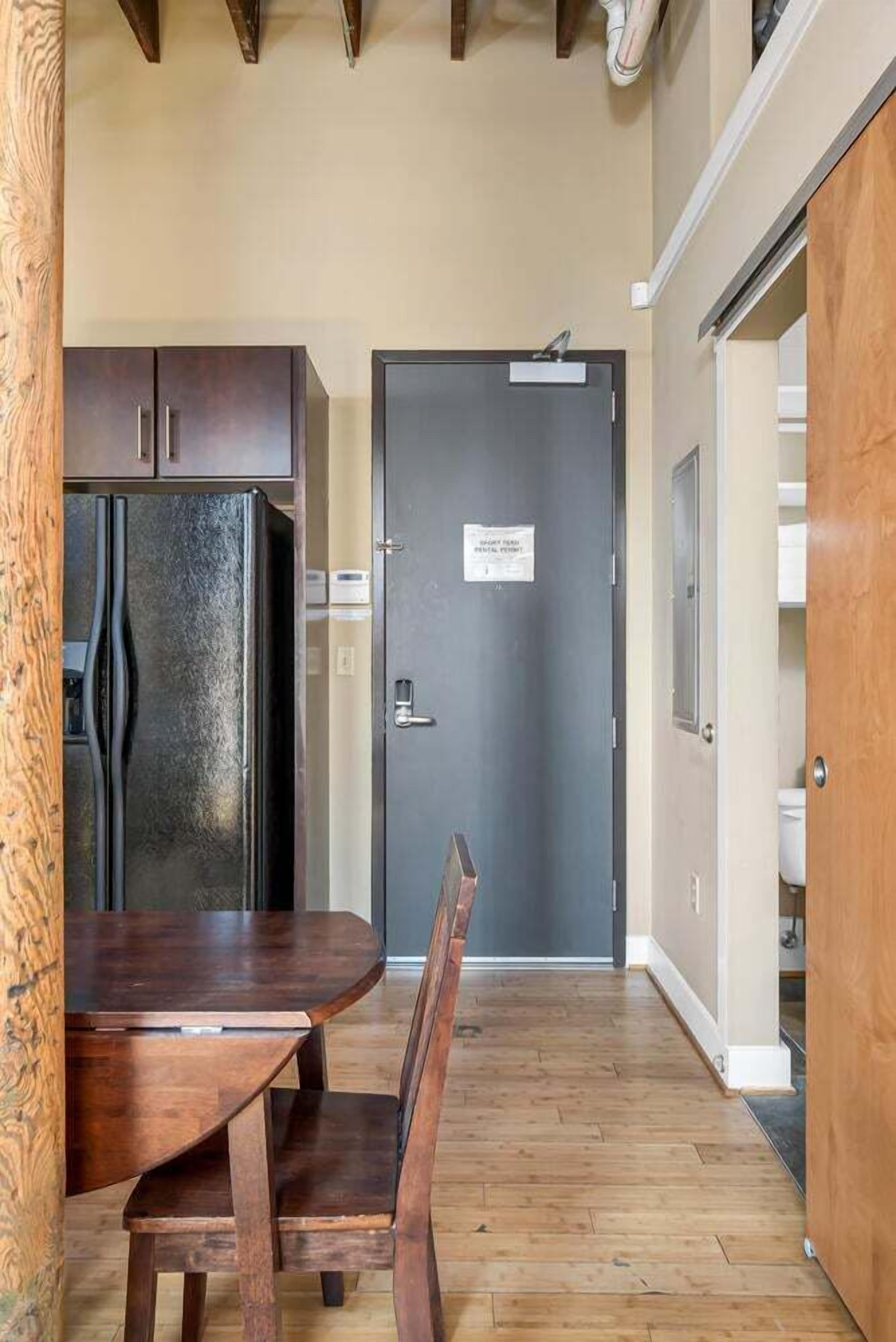 A compact kitchen with dark cabinets, a black refrigerator, and a wooden dining table with chairs.