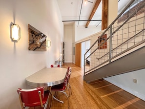 A dining area with a round table and red chairs, a wooden floor, and a staircase with metal railings.