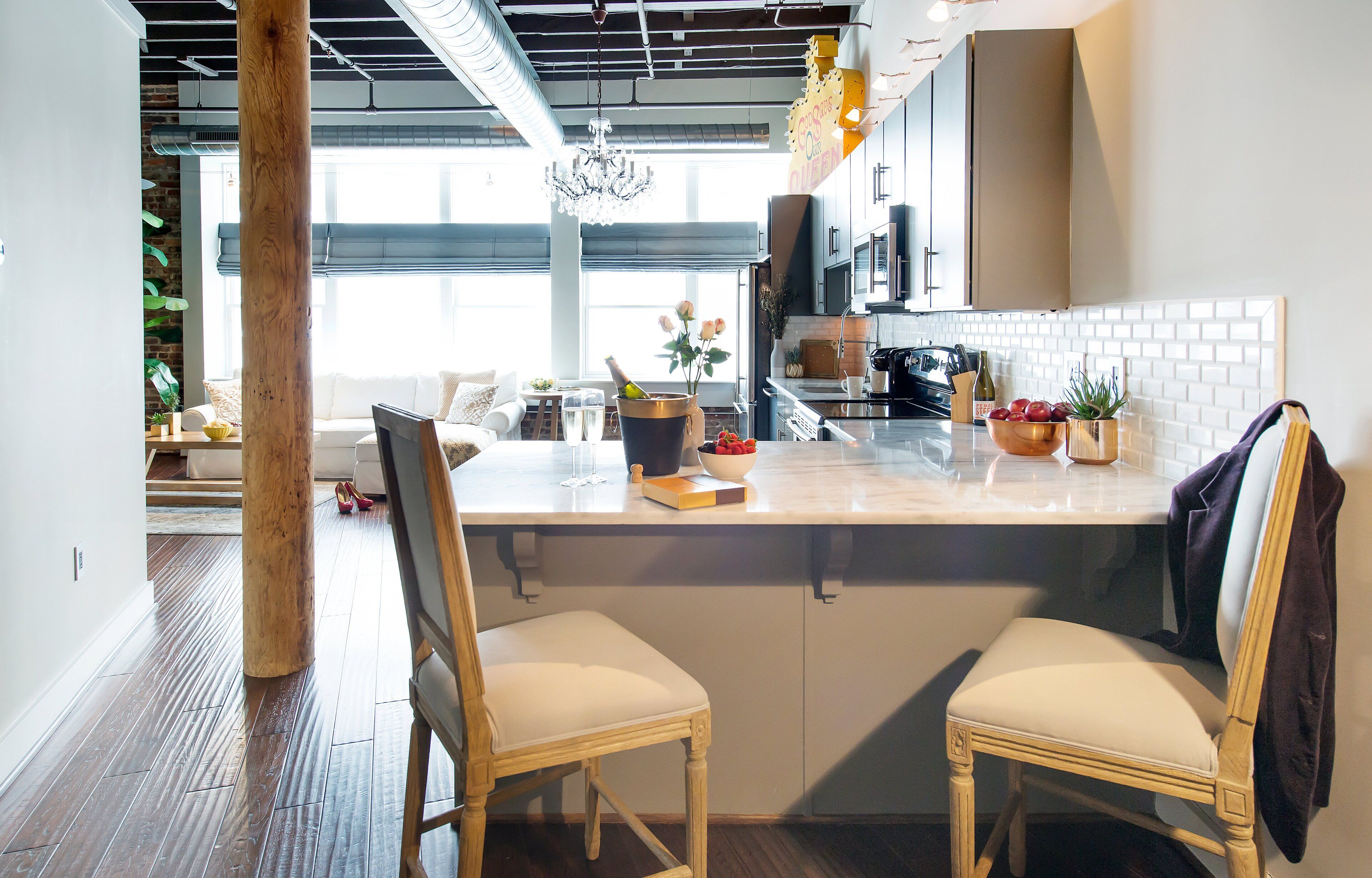 A modern kitchen with a marble countertop, wooden chairs, and a large window.
