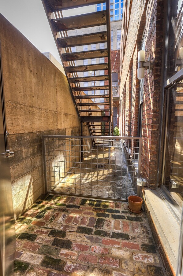 A narrow alleyway with a metal gate, brick walls, and a wooden staircase.