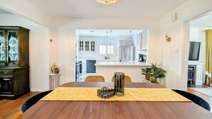 A dining area with a large wooden table, a chandelier, and a view into the kitchen. - Charming Lux Gem in Med Center w/ 2 K Beds-Patio-Backyard! (Houston)