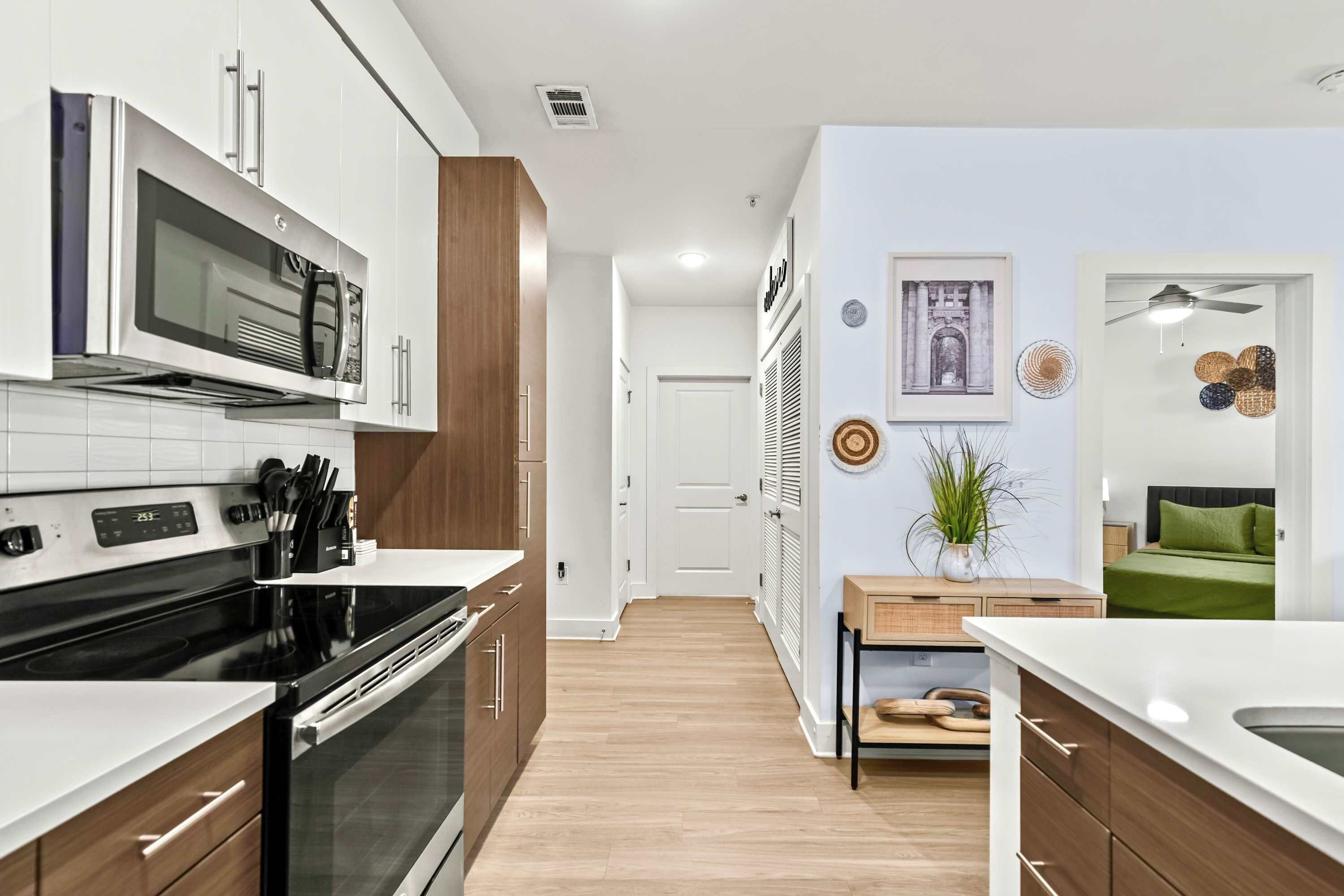 A modern kitchen with a built-in microwave, oven, and stove. There is a wooden cabinet and a white countertop. A door leads to another room.