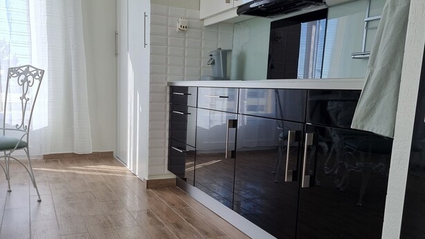A modern kitchen with white cabinets, a black countertop, and a wooden floor.