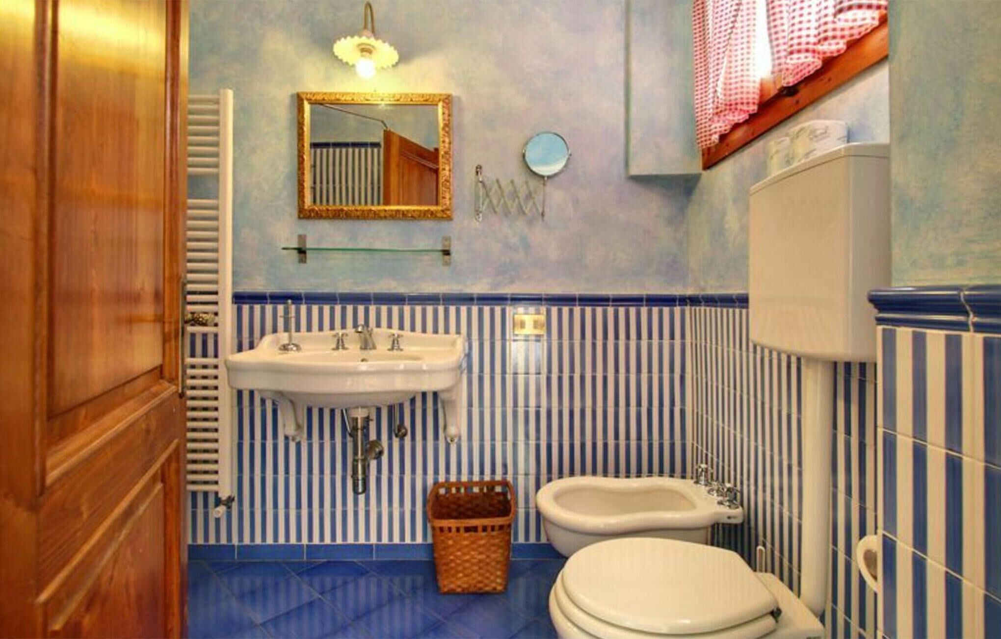 A bathroom with a sink, mirror, toilet, and a small basket on the floor.