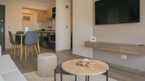 Un salon moderne avec une table ronde en bois, un canapé et un téléviseur fixé au mur.