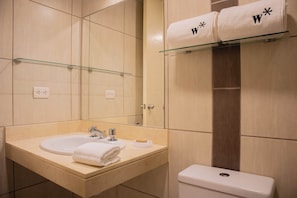 A bathroom with two sinks, a glass shelf with towels, and a toilet.