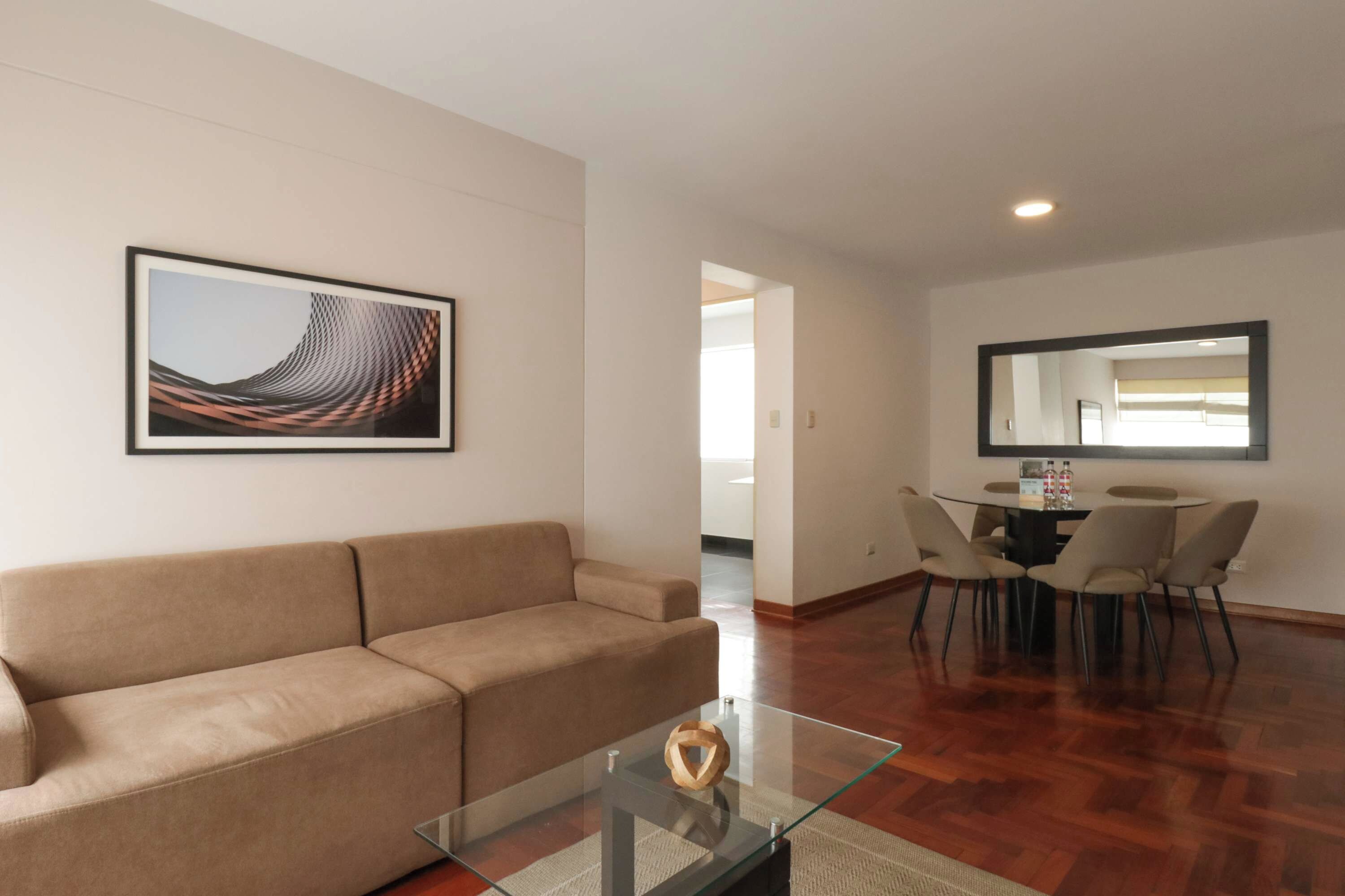 A modern living room with a sofa, a glass coffee table, and a dining area with chairs and a table.