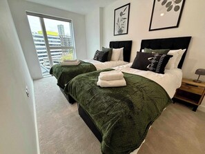Een moderne slaapkamer met twee bedden, een groot raam en uitzicht op de stad.