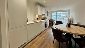 A modern kitchen with a dining area, featuring a wooden dining table and chairs, a built-in oven, and a large window with a city view. - Stylish 2BR Apt Bracknell | Near Ascot (Bracknell)