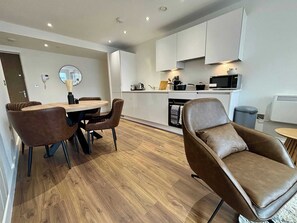 Een moderne keuken met witte kasten, een magnetron en een eethoek met een ronde tafel en bruine stoelen.