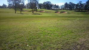 En golfbane med sandbunkere, træer og en klar himmel.