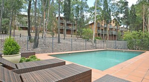 A rectangular pool with a tiled deck, surrounded by a fence and trees.