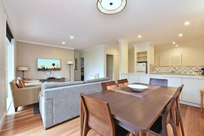 A modern living room with a sofa, TV, and dining area with a table and chairs. - Villa 2br Pinot Nois Villa (Pokolbin)