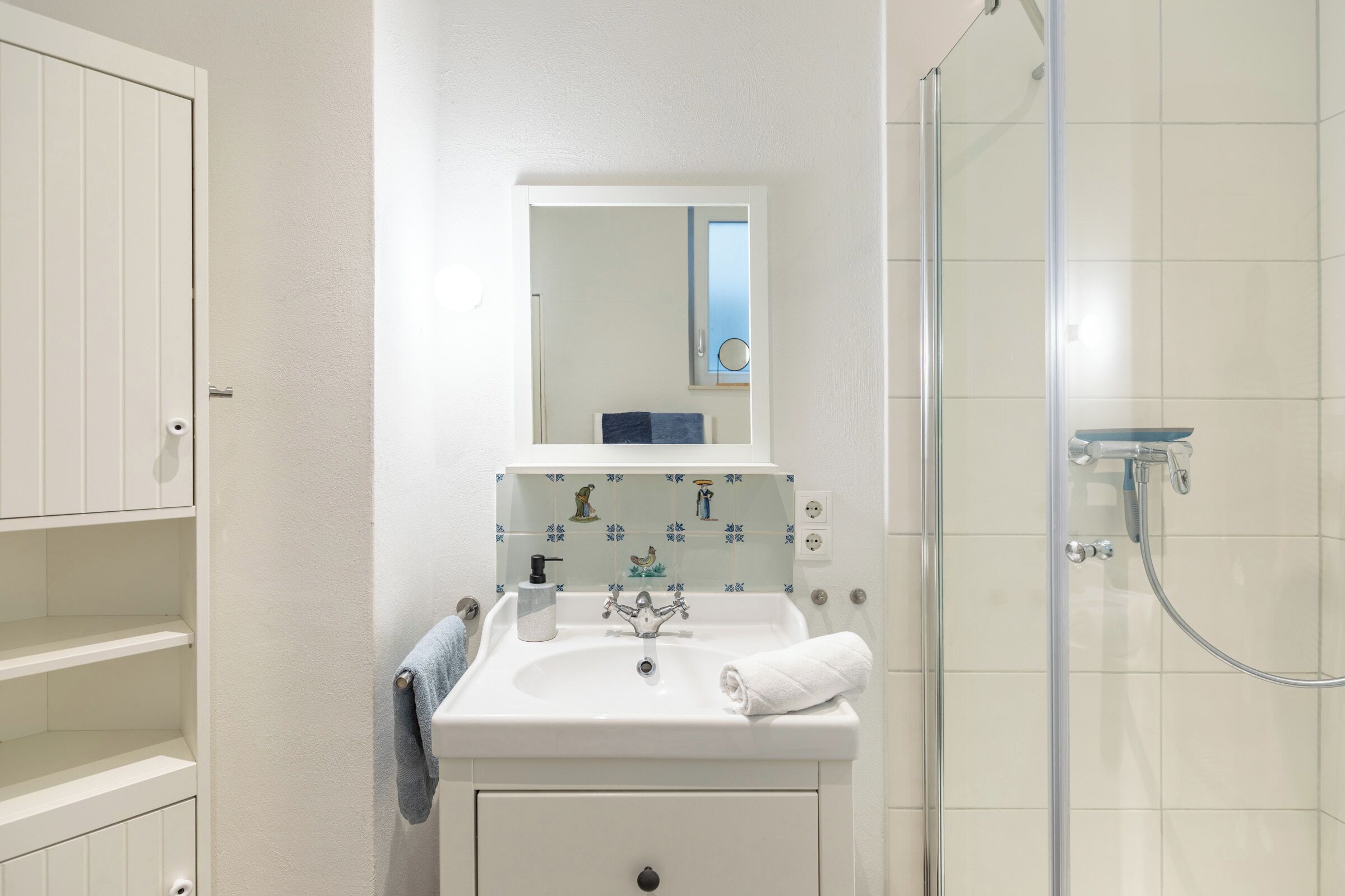 Un baño con lavamanos blanco, un espejo, una toalla y una ducha.