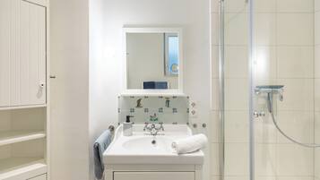 Un baño con lavamanos blanco, un espejo, una toalla y una ducha.