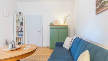 A room with a round wooden table, a blue sofa, a green cabinet, a white door, and a bookshelf.