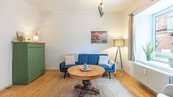 A room with a round wooden table, a blue sofa, a green cabinet, and a window with a view of a brick building.