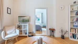 Una sala de estar con una mesa de madera, un sillón blanco, una estantería y un televisor.
